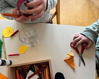 Kinderhände mit Bastelmaterialien und Scheren auf einem Tisch.