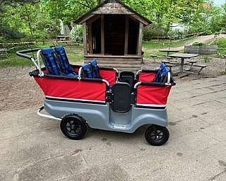 Ein roter Kinderwagen mit blauen Sitzen in einem Park.