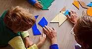 Kind und Fachkraft legen bunte geometrische Formen auf Holztisch