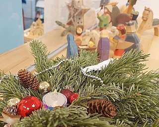 Nahaufnahme von Tannenzweigen mit Weihnachtsdekoration und Figuren im Hintergrund.