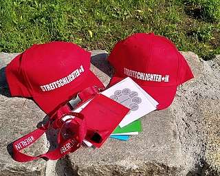 Zwei rote Kappen mit Streitlichter-Aufdruck, Ausweise und Karten auf Stein