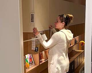 Frau in hellen Pullover misst Maße an Möbelstück im Einrichtungshaus