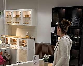 Frau in beigem Pullover betrachtet beleuchtete Küchenschränke mit Geschirr