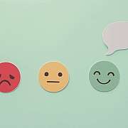 Rote, gelbe und grüne Emoticons mit Säuerausdruck, Neutral und Lächeln, darauf eine Hand mit Sprechblase
