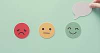Rote, gelbe und grüne Emoticons mit Säuerausdruck, Neutral und Lächeln, darauf eine Hand mit Sprechblase