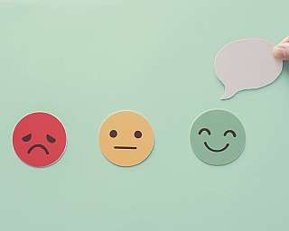 Drei runde Emoticons mit unterschiedlichen Gesichtsausdrücken und eine Hand hält eine leere Sprechblase