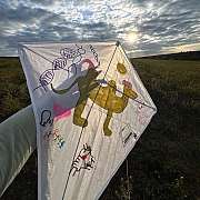 Weißer Papierdrachen mit bunten Zeichnungen gehalten bei Sonnenuntergang im Feld